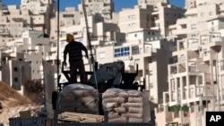 FILE - A worker stands by construction materials to unload at a new housing unit in the east Jerusalem neighborhood of Har Homa, Nov. 2, 2011.