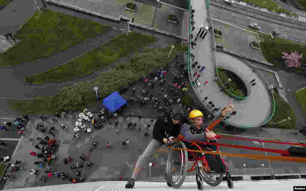 Jakub Koucky (R), a graduate from Jedlickuv Institute, in a wheelchair, is helped by a climber during the first ever attempt to rappel from Prague&#39;s Congress Center at an event to mark the institute&#39;s 100th founding anniversary in Prague, Czech Republic. 