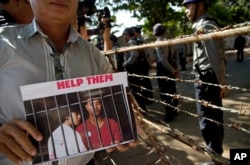 A protester displays a picture featuring Myanmar migrants Win Zaw Htun, right, and Zaw Lin near the Thai Embassy in Yangon, Myanmar, Friday, Dec. 25, 2015.