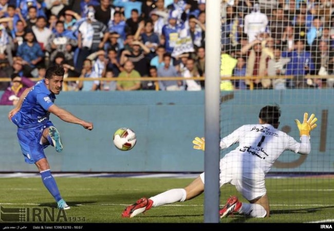 An Esteghlal player fires a shot against the Persepolis goalkeeper as spectators in the men-only stands watch two of Iran's fiercest rival football teams play at Azadi Stadium in Tehran, March 1, 2018.