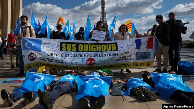 FILE - Supporters of the French Uyghur Community shout slogans and hold Uyghur flags during a demonstration over China's human rights record near the Eiffel Tower on March 25, 2019.