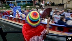 A woman fans herself to stay cool while attending the Fiesta Mariachi Festival on San Antonio's River Walk.