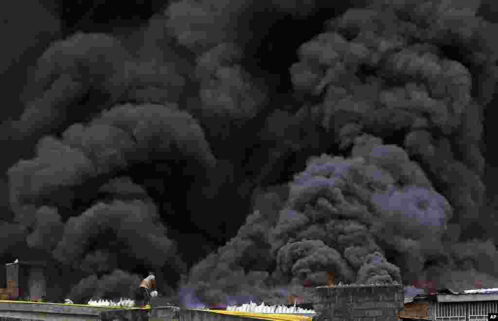 A man with a bucket tackles a blaze as smoke rises from a fire at the Balogun market in downtown Lagos, Nigeria.