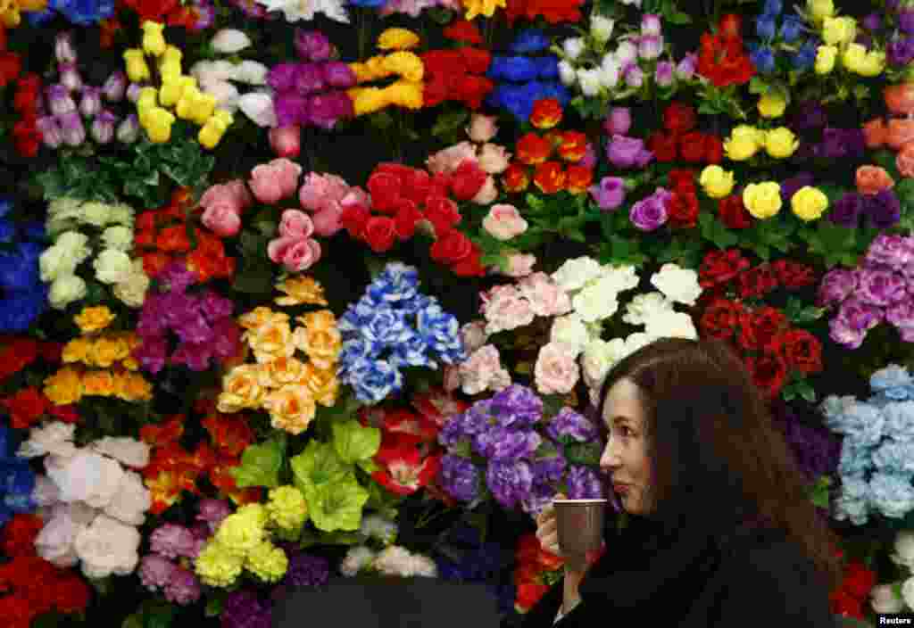 A woman drinks coffee at a stand with artificial flowers during the &quot;Memorial and Stone Working-2015&quot; exhibition in Minsk, Belarus.