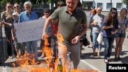 Members of a Ukrainian activist group burn goods produced in Russia as they hold a rally against what they see as undue Russian trade pressure on Ukraine, in front of Russia's Embassy in Kyiv, August 16, 2013. The sign reads: "Stop economic terror.