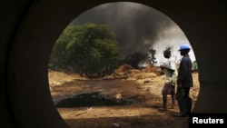 Oil workers, seen through a pipe, look on at the scene of an oil pipeline fire in Dadabili, Niger state, April 2, 2011.
