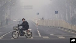 FILE - A man rides an electric bike crossing a street shrouded by haze in Beijing. 