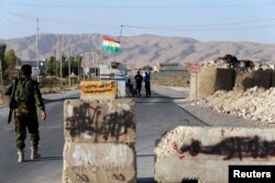 FILE - Kurdish Peshmerga fighters man a checkpoint as words written on stone slabs by the Islamic State are seen painted out, at Makhmur town, Sept. 10, 2014.