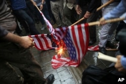 FILE - Iranian demonstrators burn representations of the U.S. flag during a protest in front of the former U.S. Embassy in response to President Donald Trump's decision to pull out of the nuclear deal and renew sanctions, in Tehran, Iran, May 9, 2018.