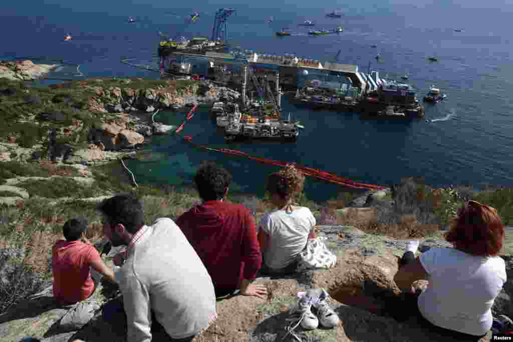 People look on as the capsized cruise liner Costa Concordia lies on its side next to Giglio Island, Italy, Sept. 16, 2013. 