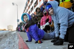 Nayla Timmer, 8, left, and Delayna Barnum, 12, of Chugiak, find a lower angle helps their view of dogs and mushers during the ceremonial start of the Iditarod Trail Sled Dog Race in Anchorage, Alaska, March 4, 2017.