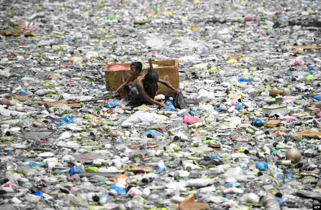 Hai cha con trên một chiếc thuyền làm bằng chất xốp chèo qua con sông đầy rác để thu thập chai nhựa bán ve chai ở Manila, Philippines.
