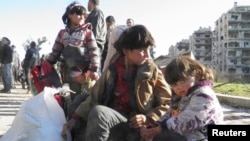 FILE - Syrian children sit with their belongings as they wait to be evacuated from a besieged area of Homs Feb. 12, 2014.