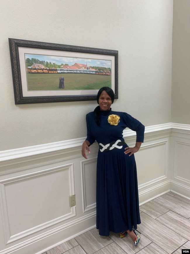 Courtney Tobias inside Life Tabernacle Church in Baton Rouge, posing in front of a photo of Pastor Tony Spell, his wife, and the church's bus fleet.