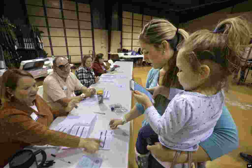 Cori Jahns menggendong putrinya Adalynn saat memberikan suaranya dalam pemilihan presiden, di TPS di Bradfordton, Illinois (8/11). (AP/Seth Perlman)
