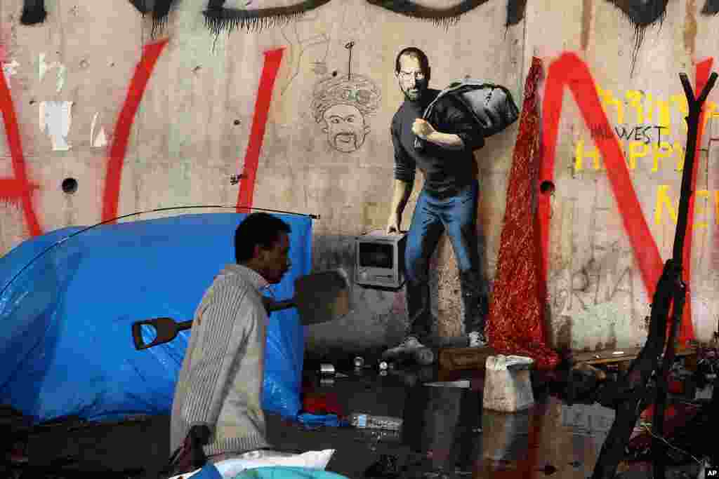 Seorang pengungsi berjalan melalui sebuah lukisan karya seniman graffiti Inggris, Banksy, di pintu masuk kamp pengungsi Calais di Calais, Perancis utara.