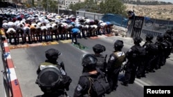 Warga Palestina melakukan shalat Jumat, sementara polisi Israel melakukan penjagaan di pinggiran Yerusalem (4/7). 