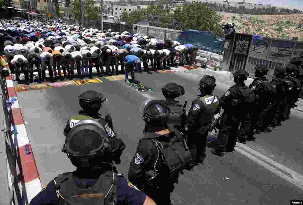 Para warga Palestina melakukan shalat Jumat pertama dalam bulan Ramadhan, disaksikan polisi Israel di daerah Wadi al-Joz, Yerusalem timur (4/7). (Reuters/Baz Ratner)