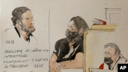 This courtroom sketch shows key defendant Salah Abdeslam, at left and in black at center, with court president Jean-Louis Peries, right, in the special courtroom built for the 2015 attacks trial, Sept. 8, 2021 in Paris, France. 