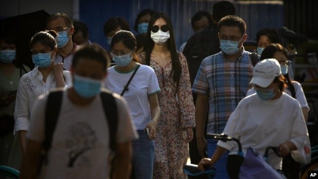 People wearing face masks to protect against the coronavirus wait to cross an intersection in the central business district in Beijing, Wednesday, July 15, 2020. China is further easing restrictions on domestic tourism after reporting no new local cases o