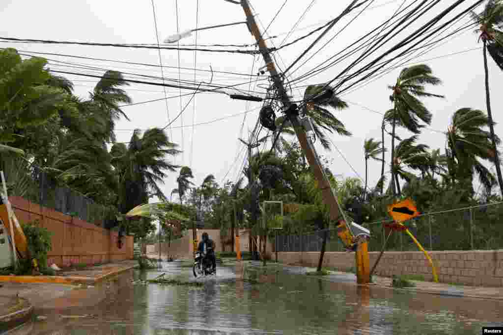 Seorang pria mengendarai sepeda motor di jalanan yang tergenang banjir pasca badai Maria melanda Punta Cana, Dominika.