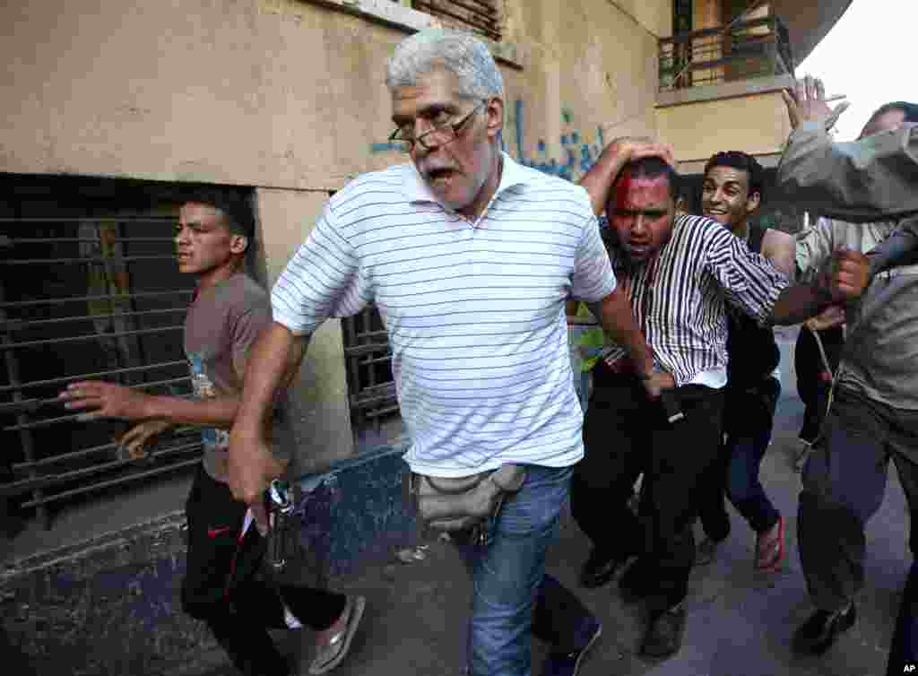 An Egyptian man with a pistol and opponents of Egypt's ousted President Mohamed Morsi detain a suspected Morsi supporter who was wounded during clashes in Cairo, July 22, 2013.