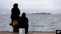 FILE - Two women sit on a dock of a refugee camp which houses about 3,200 refugees and migrants, in the western Athens suburb of Skaramagas, Aug. 25, 2016. 