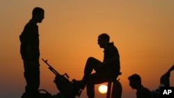 The sun sets as Israeli army soldiers stand on top of military vehicles just outside the Gaza Strip near Kibbutz Kfar Azza.