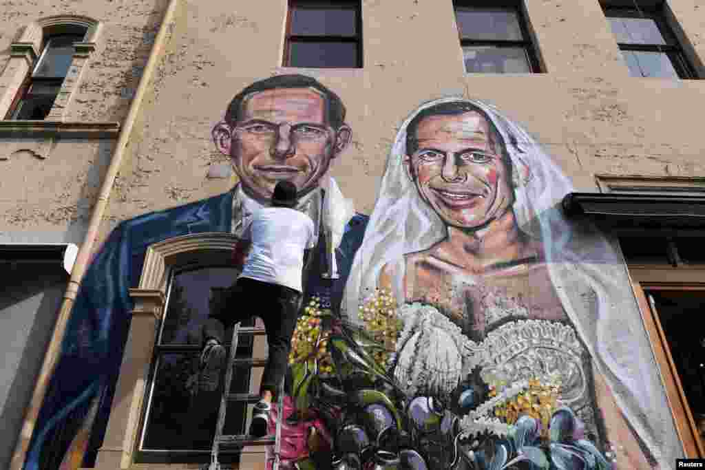 Australian artist Scott Marsh completes a mural artwork featuring the likeness of former Australian Prime Minister Tony Abbott marrying himself in a wedding dress in the Sydney suburb of Redfern, Australia.