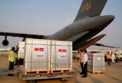 Workers stand next to the shipment of 600,000 doses of the coronavirus disease (COVID-19) vaccines donated by China at the Phnom Penh International Airport, in Phnom Penh, Cambodia February 7, 2021.