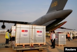 Workers stand next to the shipment of 600,000 doses of the coronavirus disease (COVID-19) vaccines donated by China at the Phnom Penh International Airport, in Phnom Penh, Cambodia February 7, 2021.