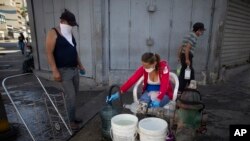 Personas usan máscaras protectoras como precaución contra la propagación del nuevo coronavirus recolectan agua de una boca de riego, en Caracas, Venezuela, el martes 17 de marzo de 2020.