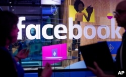 FILE - Conference workers speak in front of a demo booth at Facebook's annual F8 developer conference, in San Jose, California, April 18, 2017.