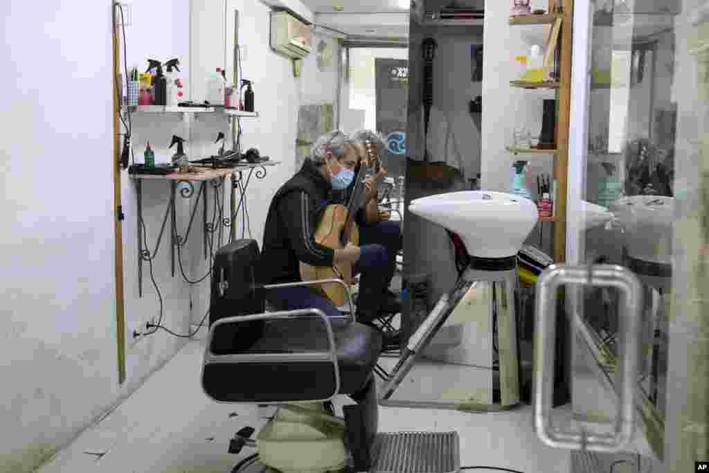 Geraldo, a barber, plays his guitar while waiting for customers, wearing a face mask to protect against the spread of coronavirus in his small hairdresser premises in Madrid, Spain, Friday, Nov. 6, 2020. Restrictions are in force across the country as aut