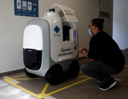 Seorang pelanggan mengambil belanjaannya yang diantar oleh robot Camello di Singapura, 6 April 2021. (Foto: Edgar Su/Reuters)