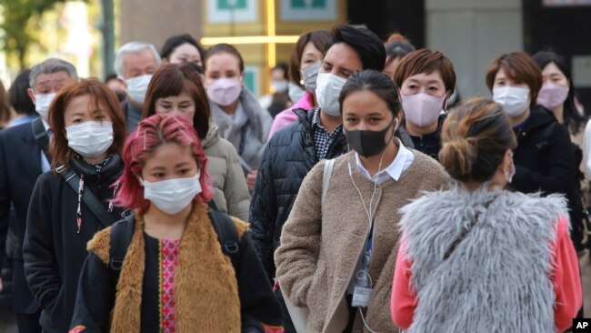 People wearing face masks to protect against the spread of the coronavirus walk along a street in Tokyo, Nov. 29, 2021.