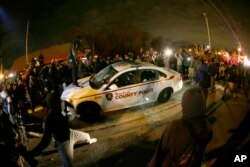 Um carro da polícia é rodeado por manifestantes em Ferguson