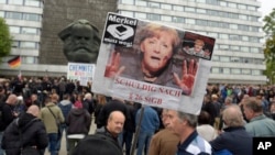 A protester holds up a poster with a photo of German Chancellor Angela Merkel declaring her "Guilty" at an anti-migrant rally in Chemnitz, eastern Germany, Sept. 1, 2018.