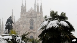 FILE - Palm trees are dusted in snow after a snowfall in front of Milan's Gothic Cathedral, Italy, March 2, 2018. New U.S. weather data shows that the Arctic just finished its warmest winter on record, with plenty of open water where the ocean normally freezes.