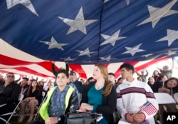 FILE - New citizens and their families look on as a large American flag is passed overhead during a U.S. Citizenship and Immigration Services naturalization ceremony, Jan. 19, 2018, in Biscayne National Park, Fla. Eighty-three children from 17 countries became American citizens during the ceremony.