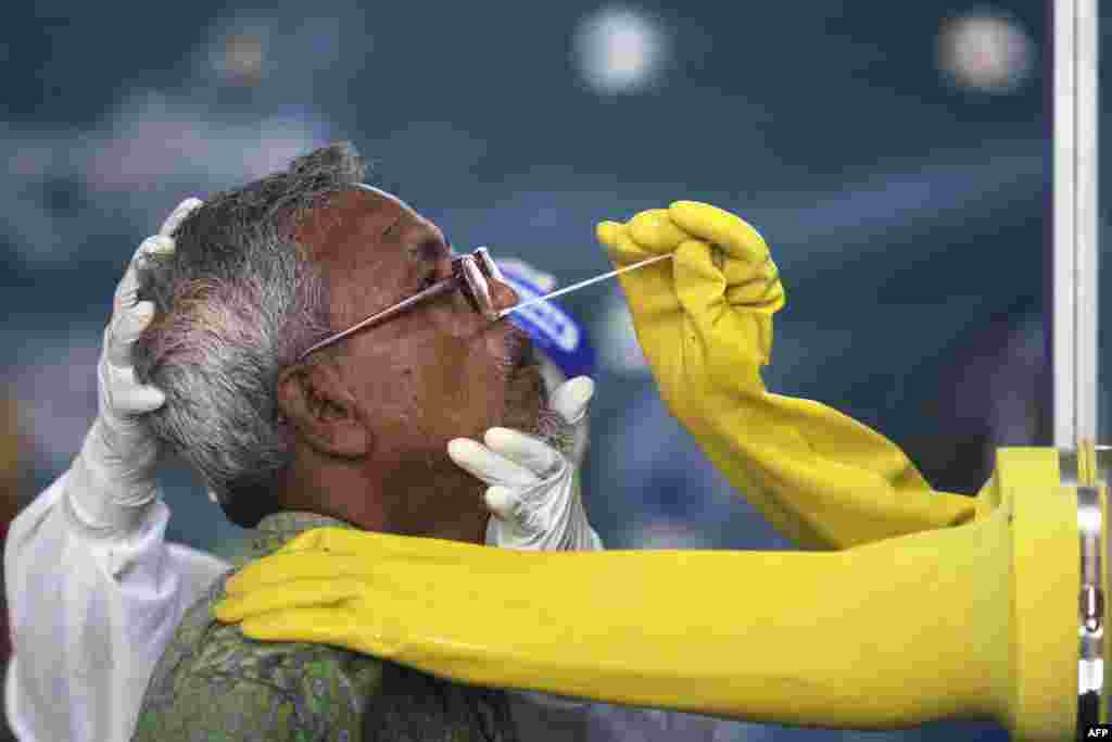 An employee of the Mugda Medical College and Hospital collects a swab sample from a resident to test for the COVID-19, in Dhaka, Bangladesh.