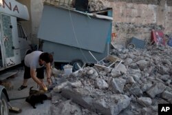 A woman feeds puppies next to rubble, following an earthquake at the port of Kos island, Greece, July 22, 2017.