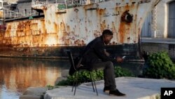 FILE - A migrant uses his mobile phone as he sits on a dock of Valletta harbor, Malta, Feb. 2, 2017.