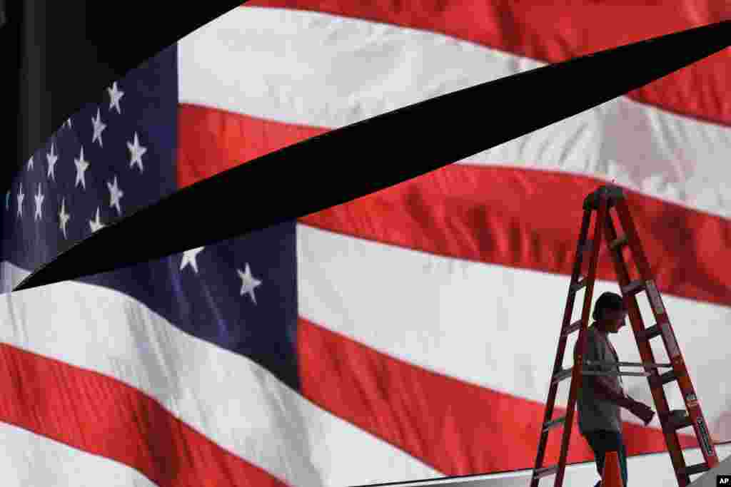 Adam West prepares to move a ladder from in front of the stage screen that displays an American flag as preparations continue for the Republican National Convention, at the Quicken Loans Arena in Cleveland.