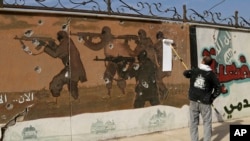 FILE - A volunteer begins to paint over a mural that had been displayed by the Islamic State group, on the eastern side of Mosul, Iraq.
