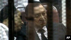 FILE - Ousted Egyptian President Hosni Mubarak, sits in the defendants cage behind protective glass, during a court hearing as he listens to his son Gamal, left, in Cairo, Egypt, May 2014.