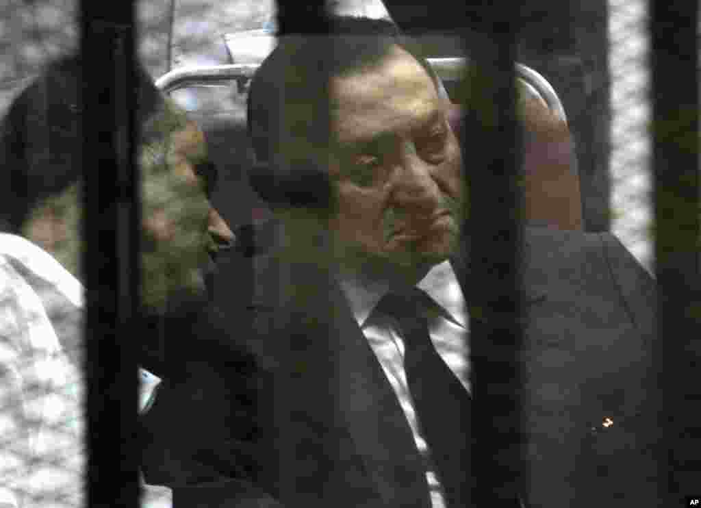 Ousted Egyptian president Hosni Mubarak sits in the defendant cage as he listens to his son Gamal (left) during a court hearing in Cairo, Egypt, May 21, 2014.