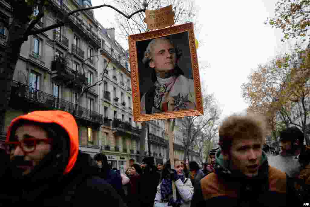A woman holds a picture of French President Emmanuel Macron painted as a member of royalty, during a demonstration against changes to the French retirement system, in Paris.