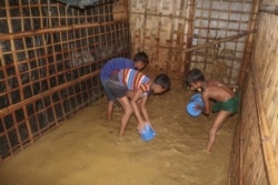 Rohingya refugee children try to pour away flood water from their homes at the Rohingya refugee camp in Kutupalong, Bangladesh, Wednesday, July 28, 2021
