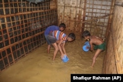 Rohingya refugee children try to pour away flood water from their homes at the Rohingya refugee camp in Kutupalong, Bangladesh, Wednesday, July 28, 2021